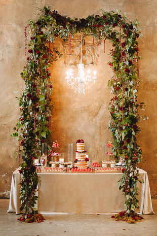 Fermenting Cellar Toronto Wedding Photographer. Floral wreath and chandelier envelope the wedding cake and sweets table.